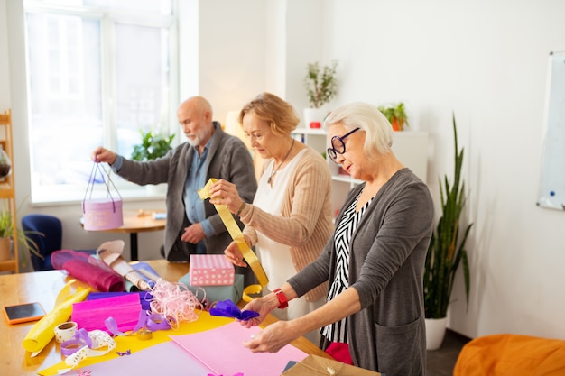 Processus créatif. Belles personnes âgées debout à table tout en utilisant le papier d'emballage