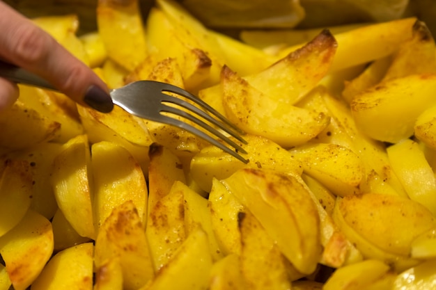 Processus de cuisson des pommes de terre au four. Une main féminine avec une fourchette pique un morceau de pomme de terre. Les tranches de pommes de terre se bouchent.