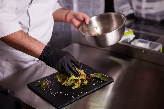 processus de cuisson de la salade tiède au veau. Mains d'un chef en gants noirs. Planche d'ardoise noire.