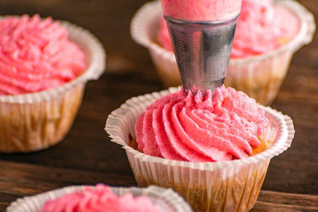 Processus de décoration de cupcakes fraîchement cuits avec de la crème rose. Gâteaux à la crème de baies. Fermer