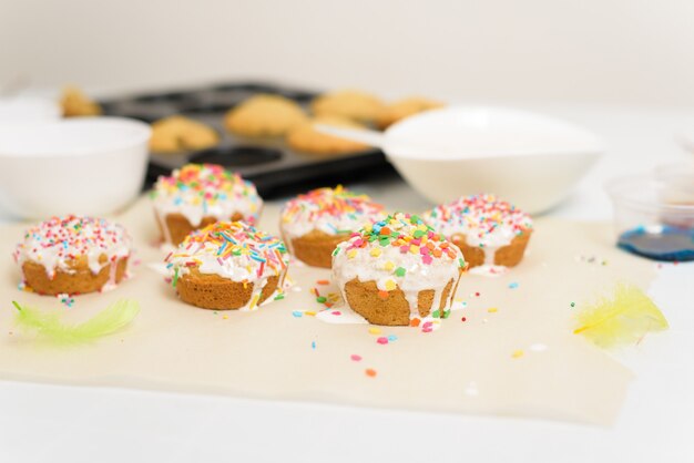 processus de décoration de mini cupcakes gâteaux de Pâques avec glaçage blanc et bonbons sucrés, vue de dessus, branches de saule et œufs à colorier.