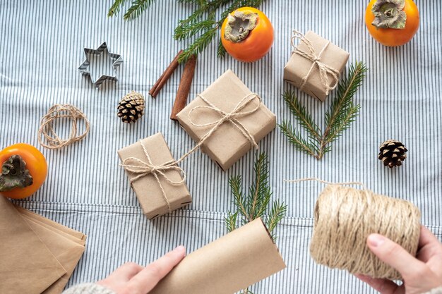 Le processus d'emballage de cadeaux modernes et élégants pour Noël et le nouvel an. Coffrets cadeaux en papier Kraft, ficelle et branches de sapin de Noël. Fond de Noël, ambiance de vacances.