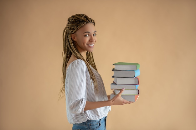 Photo processus d'étude. heureuse jeune femme afro-américaine transportant une pile de livres en face d'elle