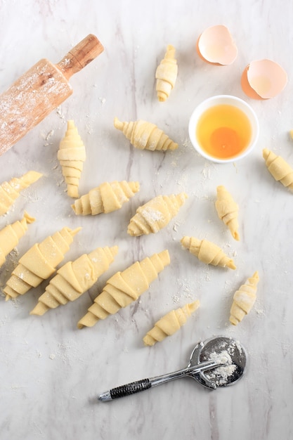 Processus de fabrication de croissants faits maison, croissants de différentes tailles au-dessus d'une table en marbre blanc