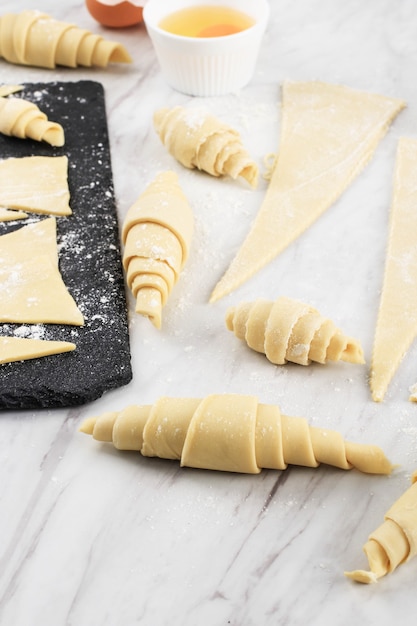 Processus de fabrication de croissants faits maison, préparation de croissants crus, cuisson à la maison. Croissant De Différentes Tailles Au-dessus De Table En Marbre Blanc