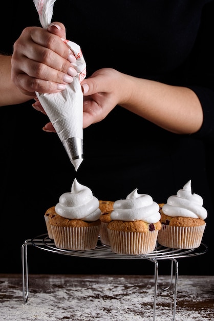 Le processus de fabrication de petits gâteaux, enrobant une crème d’un sac à pâtisserie entre les mains d’un pâtissier.