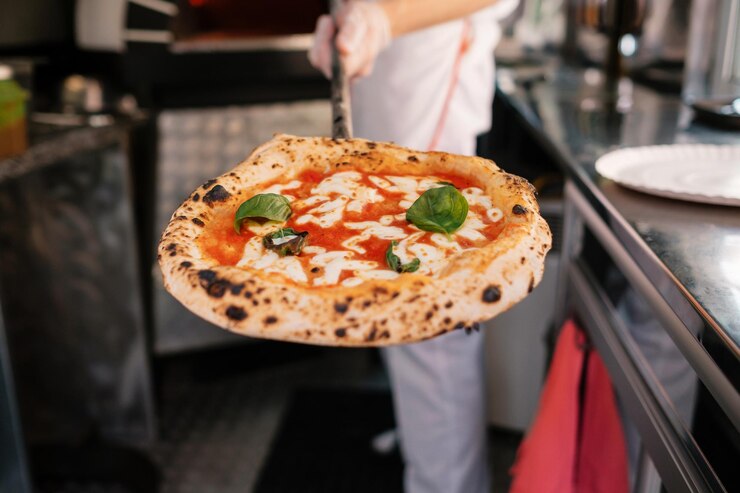 Le processus de fabrication de la pizza Le cuisinier montre la pizza qu'il a sortie d'un four à bois