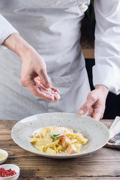 Processus de fabrication d'un plat de pâtes. Le chef saupoudre les pâtes italiennes de fromage râpé.