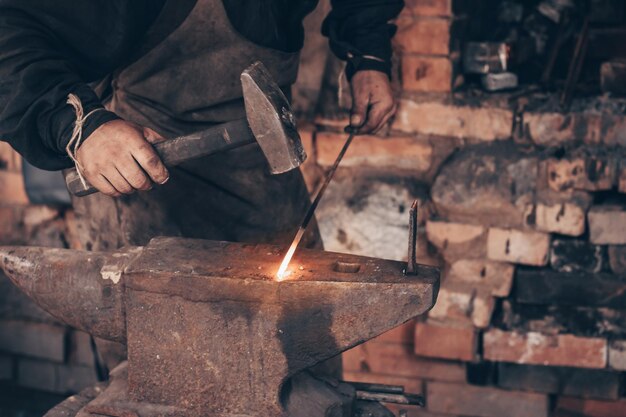 Processus de forgeron métal brillant avec un marteau sur l'enclume dans la forge Mains sales du maréchal-ferrant dans l'atelier