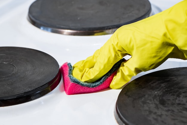 Le processus de lavage d'une cuisinière électrique. Une main dans un gant jaune nettoie la surface blanche de la saleté.