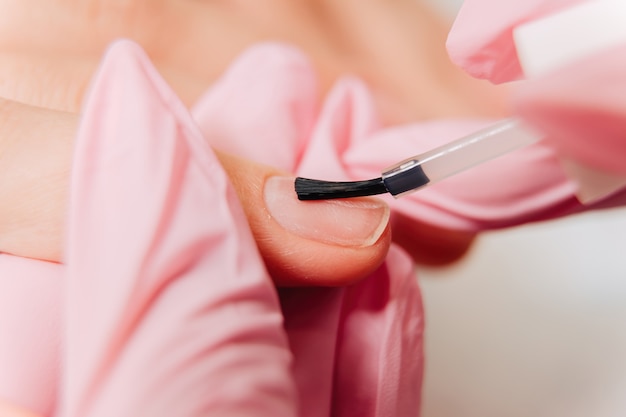 Processus de manucure. Le maître peint les ongles avec un vernis transparent