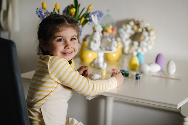 Le processus de peinture d'œufs par une petite fille sur la cuisine Décoration de Pâques des vacances de printemps à la maison vue latérale