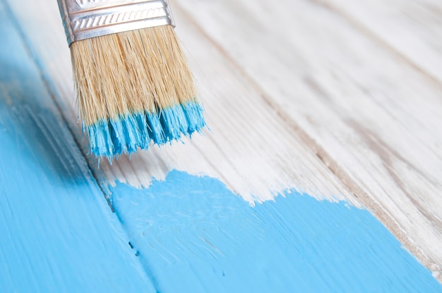 Le processus de peinture avec un pinceau de vieilles planches blanches avec vue de côté de peinture bleue