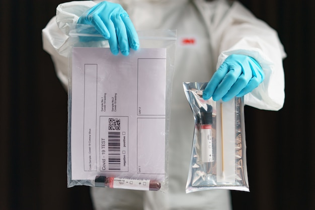 Processus de test du coronavirus, une main tient un tube d'échantillons de test sanguin et un test d'échantillon de kit de prélèvement d'écouvillon.