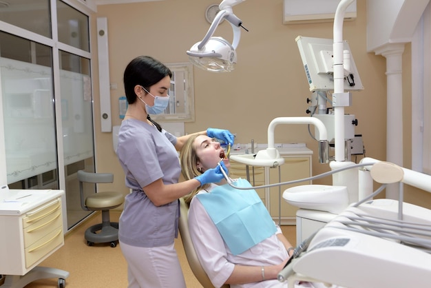 Le processus de traitement dentaire dans une clinique dentaire Femme dentiste et jeune patiente dans le fauteuil dentaire