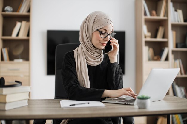 Processus de travail au bureau d'une jeune fille musulmane sérieuse ayant un appel téléphonique avec des partenaires