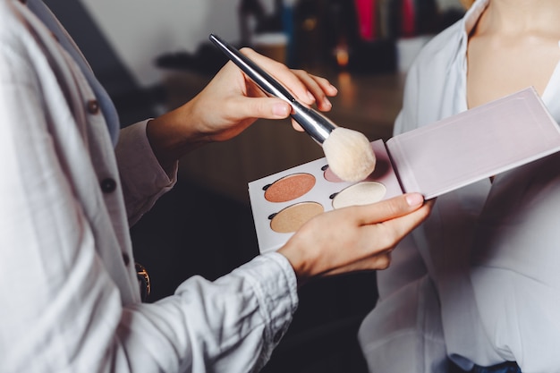 Processus de travail : maquilleuse utilisant une palette de surligneurs multicolores et un pinceau naturel et maquille une femme