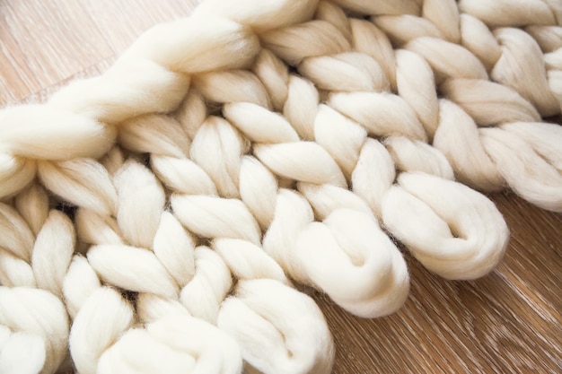 Le processus de tricotage d'un plaid de gros tricot à partir de laine mérinos. Travail inachevé avec des boucles ouvertes sur le plancher en bois