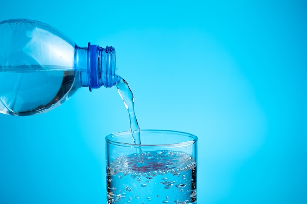 Photo le processus de verser de l'eau dans un verre sur un fond bleu