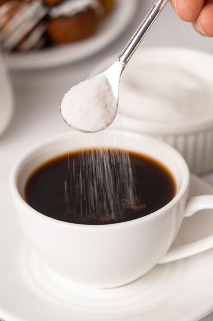 Le processus de verser le sucre d'une cuillère dans une tasse de café blanche