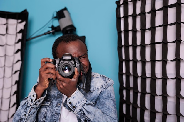 Producteur prenant des photos en se tenant debout sur fond bleu avec du matériel de photographie. Photographe professionnel prenant des photos en se tenant debout dans un studio de production équipé de lumières et de softboxes.