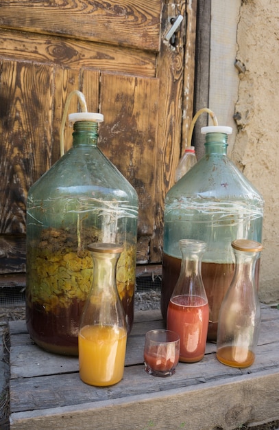 Photo production de vin fruité domestique. deux grandes bouteilles en verre avec des fruits à l'arrière-plan d'une porte en bois