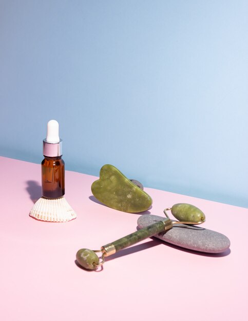 Produit cosmétique dans une bouteille en verre avec une pipette et un grattoir et un rouleau gua sha e. Pierres lisses à proximité. Le concept de soins de la peau, la cosmétologie.