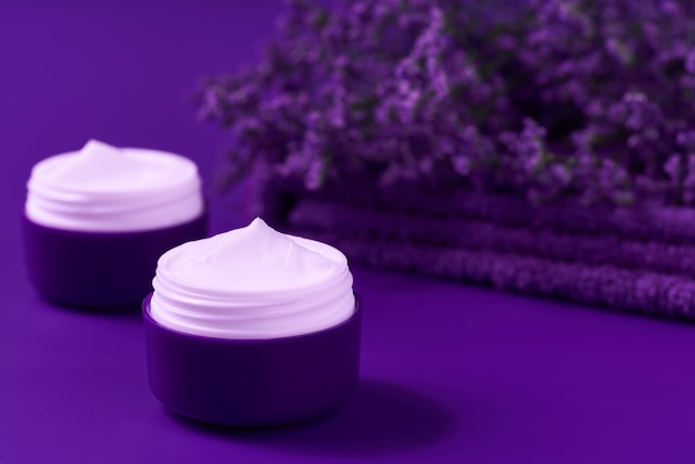 Produit de soin crème hygiénique de nuit dans un pot en plastique violet avec une serviette sur la table. Crème cosmétique nettoyante pour la peau ou lotion spa vitaminée, un hydratant anti-rides à base de plantes biologique naturel.