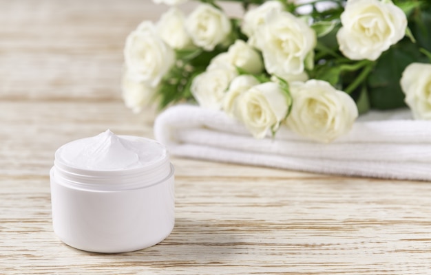 Produit de soin naturel de luxe pour le visage dans un pot en plastique blanc avec une serviette sur une table en bois. Pot blanc en plastique de crème pour la peau sensible sur une table en bois.