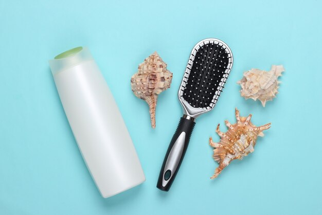 Produits de beauté pour le bain. Bouteille de shampoing, coquillages, serviette, brosse à cheveux sur fond bleu. Soin des cheveux