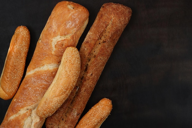 Produits de boulangerie sur l'arrière-plan d'une vue de dessus de table sombre en bois Baguettes petits pains au sésame et pain long pâtisseries croustillantes parfumées fraîches