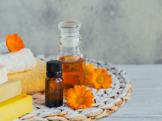 Produits de calendula. Bouteilles d'huile cosmétique, aromatique ou essentielle et fleurs de calendula fraîches sur fond clair