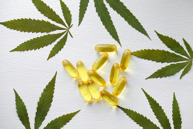 Produits de cannabis médical, feuille, capsules d'huile de CBD sur fond blanc. Gélules pharmaceutiques de gélatine à base de plantes biologiques. Concept de compléments alimentaires bio