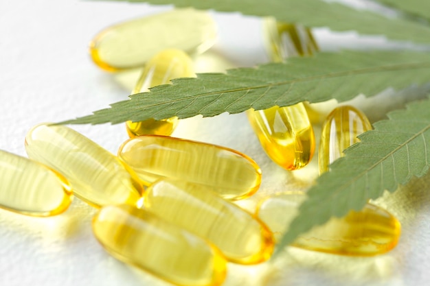 Produits de cannabis médical, feuille, capsules d'huile de CBD sur fond blanc. Gélules pharmaceutiques de gélatine à base de plantes biologiques. Concept de compléments alimentaires bio