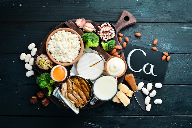 Produits contenant du calcium naturel : fromage, lait, parmesan, crème sure, poisson, amandes, persil, ail, brocoli. Sur un fond en bois noir. Vue de dessus. Espace de copie gratuit.