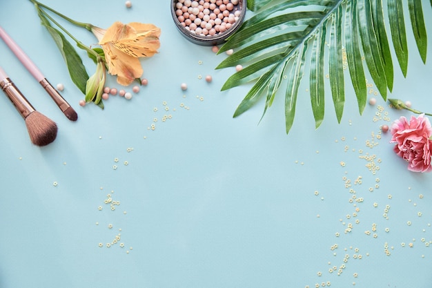 Produits cosmétiques accessoires pinceaux pour maquillage et poudre Décorations de fleurs Concept de beauté Vue de dessus copie espace fond bleu Photo de haute qualité