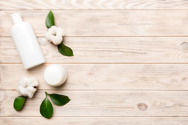 Produits cosmétiques bio avec fleur de coton et feuilles vertes sur fond de bois Copier l'espace à plat