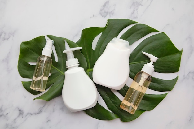 Produits cosmétiques blancs vierges sur fond de marbre avec feuille de palmier tropical