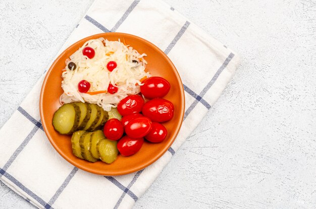 Produits fermentés faits maison sur une assiette, choucroute, tomates marinées, cornichons, fond gris clair.