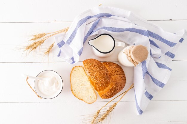 Produits laitiers frais une miche de pain un bouquet d'épis de maïs pour la célébration du shavuot juif vue de dessus fond blanc en bois