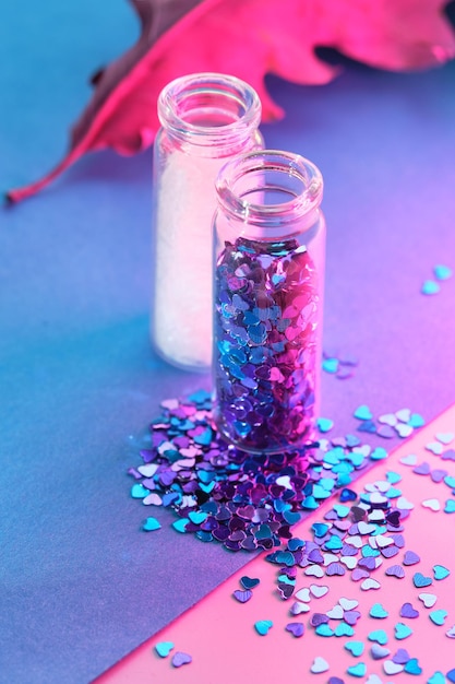 Produits de paillettes en poudre de couleur néon sur fond rose étincelant Gros plan sur des bouteilles de flacons avec diverses paillettes dans des tons rose bleu et turquoise