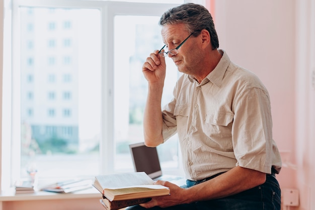 Professeur d'âge moyen dans des verres assis et lisant un manuel.