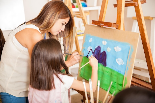 Professeur d'art mignon et une petite fille peignant ensemble un paysage à l'école