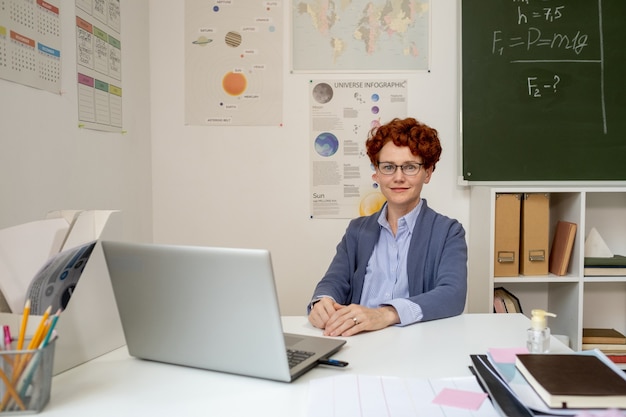 Professeur d'école en vêtements décontractés intelligents assis par bureau devant un ordinateur portable