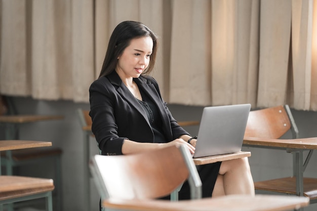 Professeur de femme asiatique gaie et confiante adulte en uniforme de costume noir avec tablette numérique et ordinateur portable enseignant moderne en classe