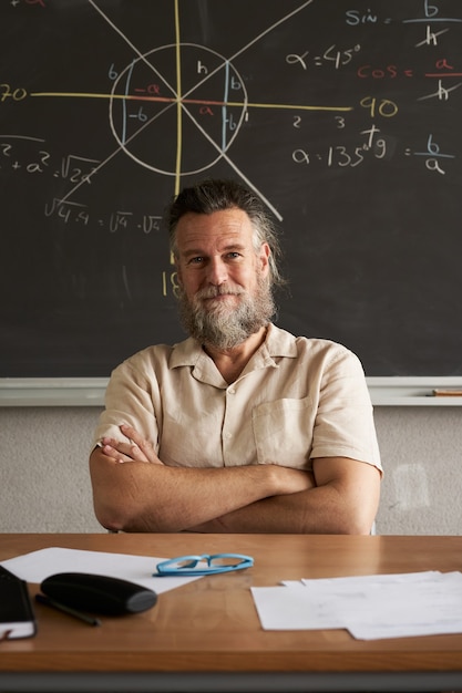 Un professeur gai de photo verticale regarde la caméra avec ses bras croisés en classe de mathématiques