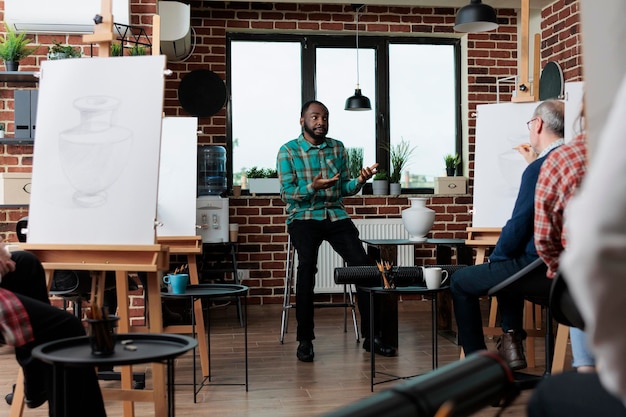 Professeur de peintre expliquant dessiner l'illustration aux étudiants en art, enseignant le processus de croquis ayant un modèle de vase pour l'inspiration. Groupe multiethnique de personnes créatives développant des compétences artistiques