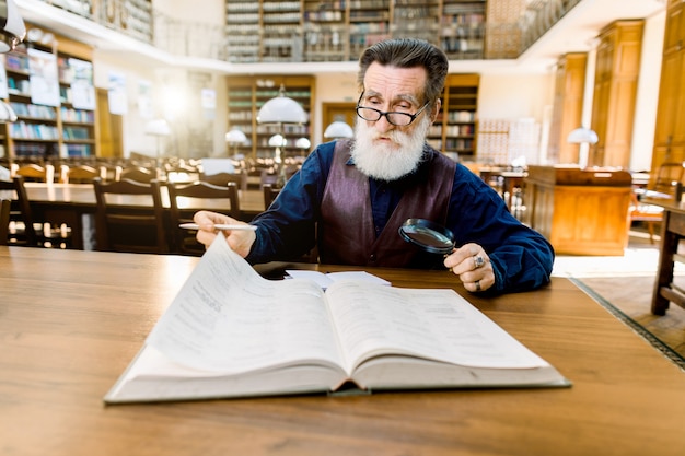 Un professeur de professeur de vieil homme, dans des vêtements vintage décontractés élégants assis à la table dans l'ancienne bibliothèque et livre de lecture. Éducation, concept de bibliothèque