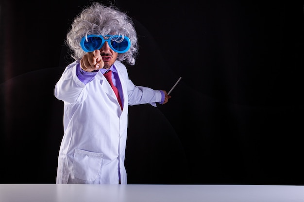 Professeur de sciences en colère en blouse blanche avec des cheveux hirsutes dans des lunettes drôles avec son doigt sur fond noir