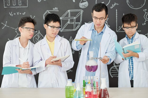 Professeur de sciences démontrant une réaction chimique aux étudiants, qui prennent des notes lorsqu'il verse du réactif dans un flacon de laboratoire